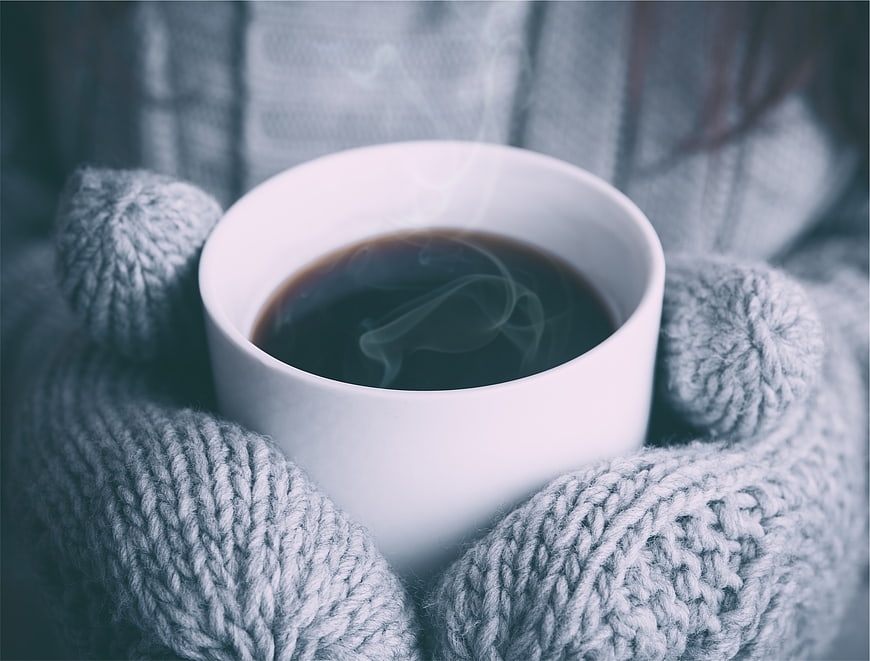 Hands in Knitted Mittens Holding Steaming Coffee Cup