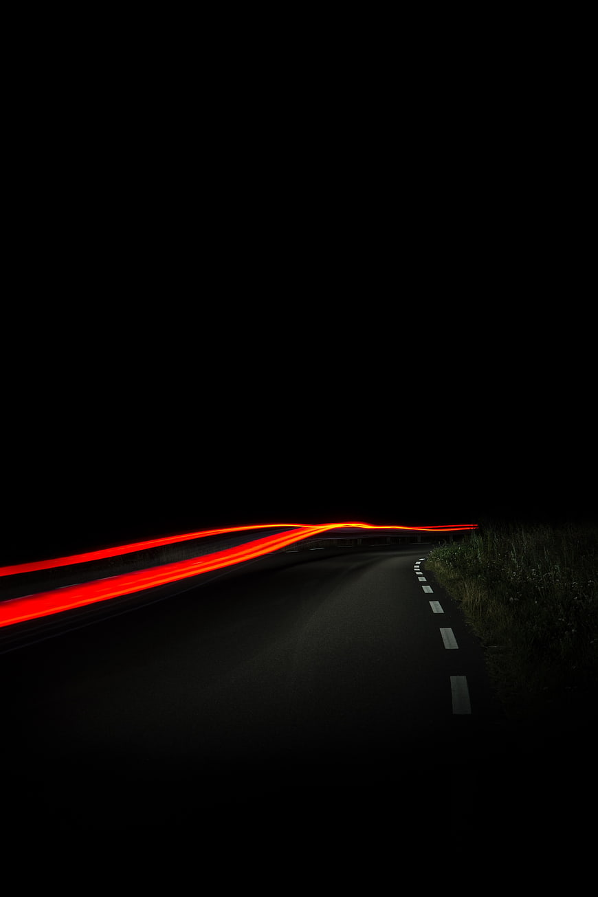 Red car light trails on dark winding road at night