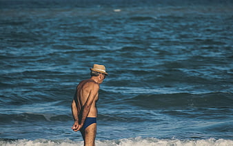 Senior man in straw hat standing by ocean waves