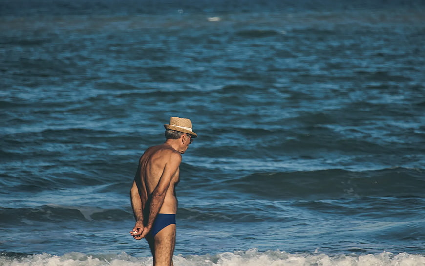 Senior man in straw hat standing by ocean waves