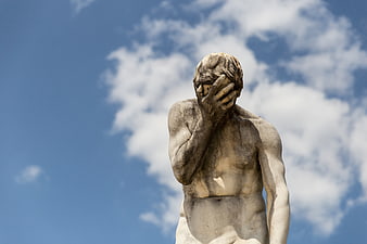 Stone Statue Facepalm Gesture Against Blue Sky