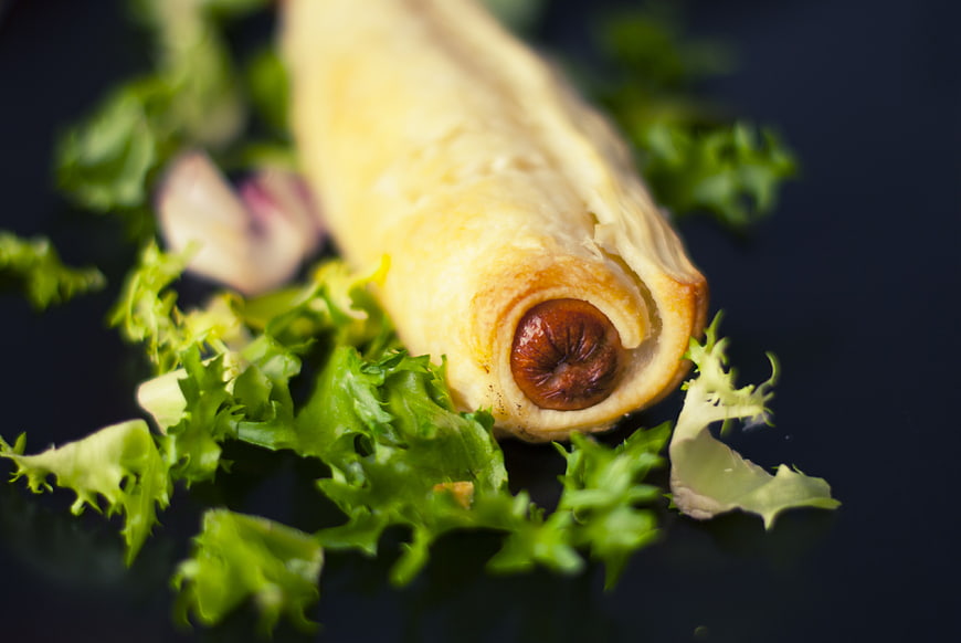 Close-up of a golden pastry-wrapped sausage on dark background