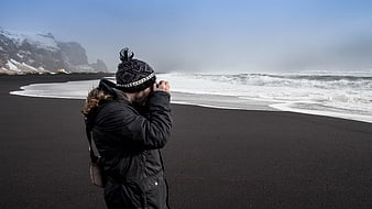 Photographer capturing waves on black sand beach