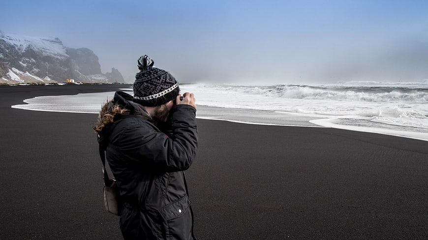 Photographer capturing waves on black sand beach
