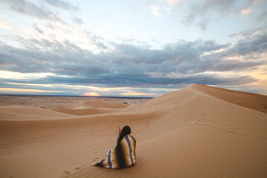 Woman Sitting on Sand Dune Watching Sunset in Desert