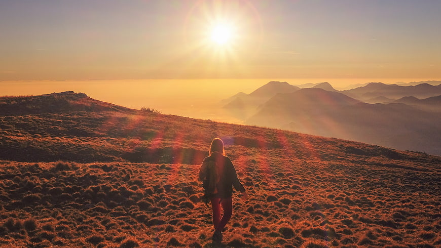 Woman hiking mountain ridge at golden hour sunset
