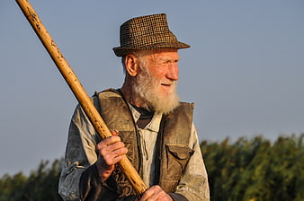 Senior man with white beard holding wooden tool in field