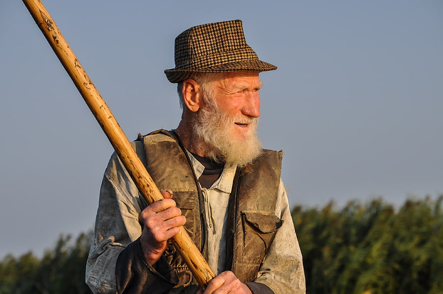 Senior man with white beard holding wooden tool in field