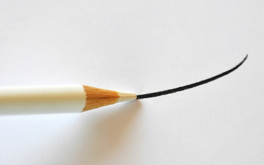 Close-up of a pencil drawing a curved line on white paper