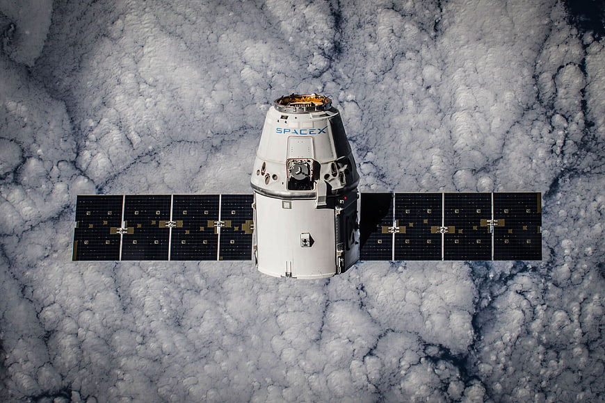 SpaceX Dragon spacecraft orbiting Earth above clouds