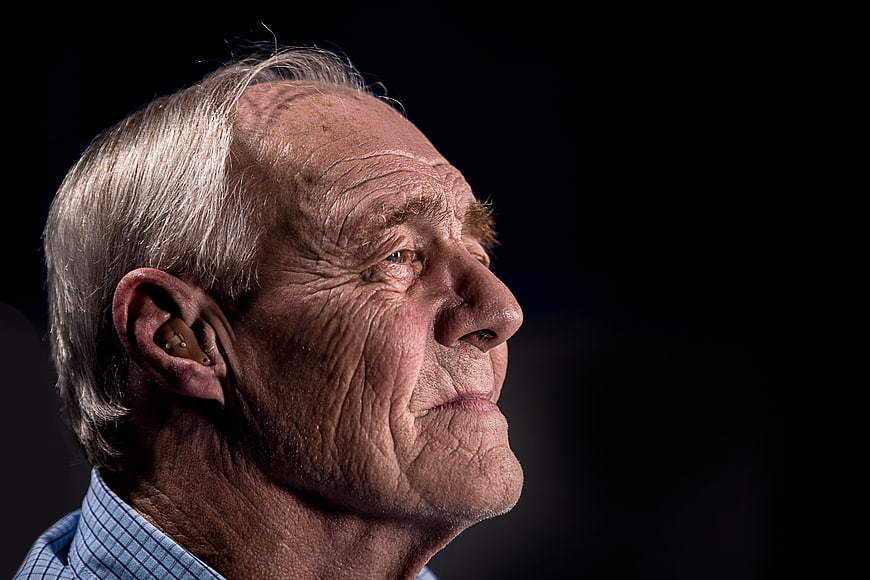 Senior man with hearing aid in profile against black background