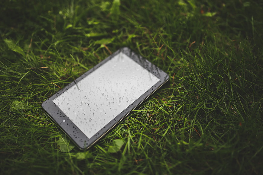Wet tablet computer lying on green grass
