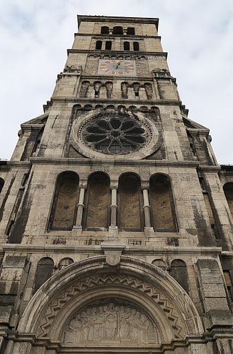 Low angle view of historic stone church tower with clock and rose window