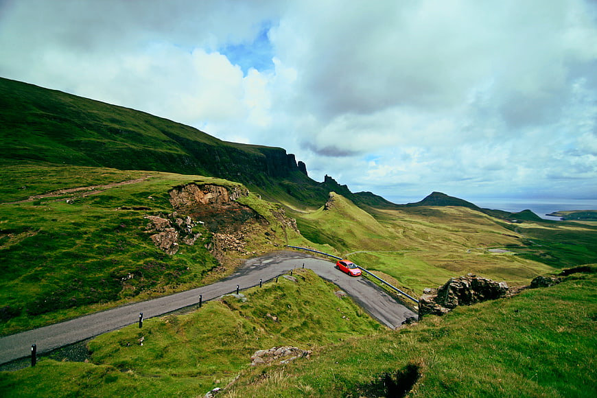 Red car driving on winding road in green highlands