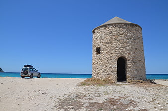 Ancient Stone Tower on Sandy Beach with SUV and Blue Sea