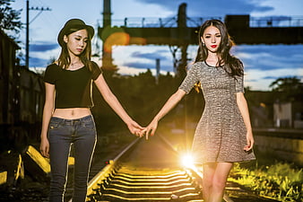 Two Young Asian Women Holding Hands on Railway Tracks at Sunset
