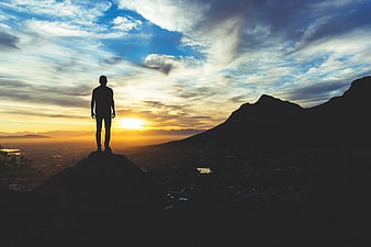 Silhouette of Man Standing on Mountain Peak at Sunset