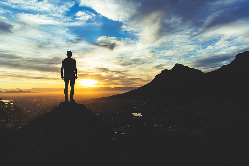 Silhouette of Man Standing on Mountain Peak at Sunset