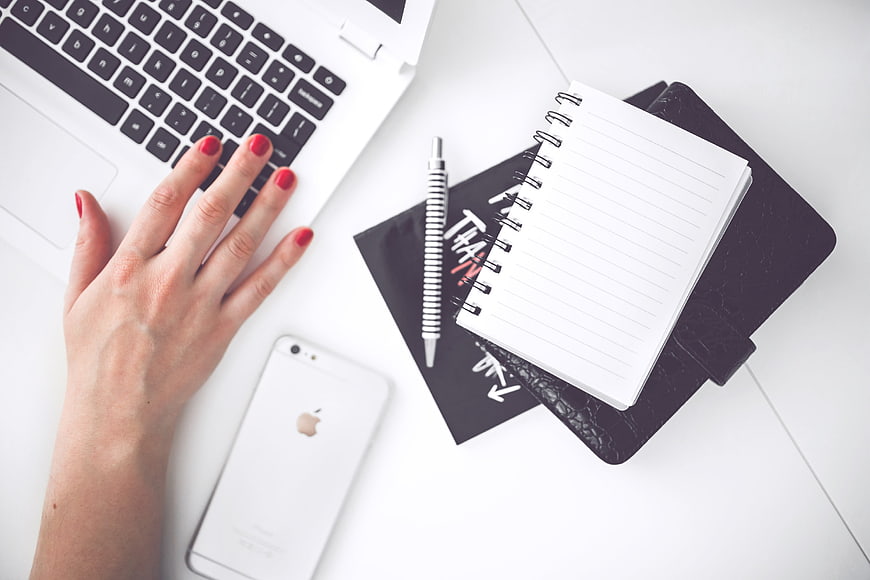 Flat lay of female hand typing on laptop with notebook and smartphone