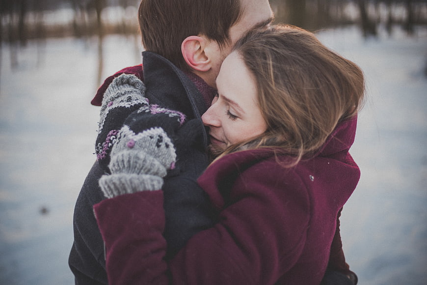 Couple Hugging in Winter Snow with Knitted Mittens