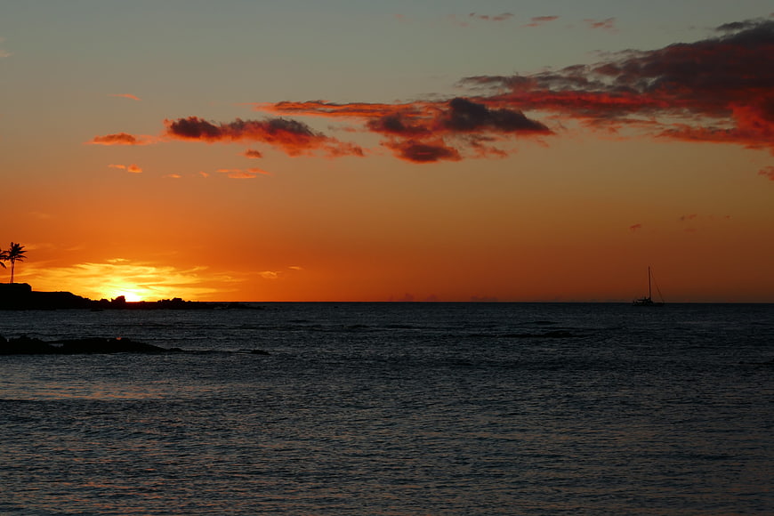 Vibrant orange sunset over ocean with sailboat silhouette