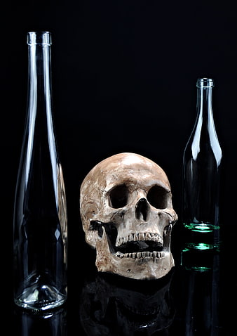 Human skull with empty glass bottles on black background