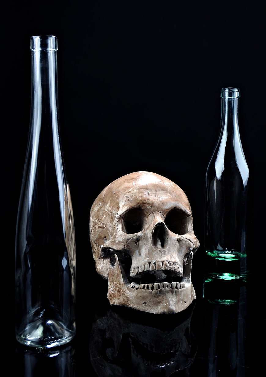 Human skull with empty glass bottles on black background