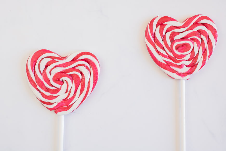 Two Heart-Shaped Pink and White Swirl Lollipops on White Background