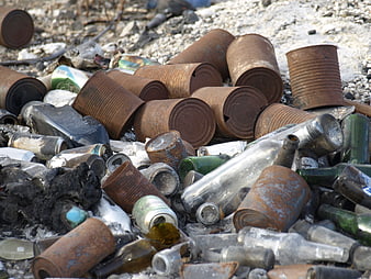 Pile of rusty metal cans and broken glass bottles in trash