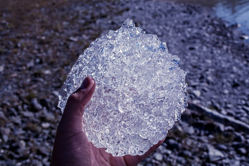 Hand Holding Large Clear Ice Chunk on Rocky Shore
