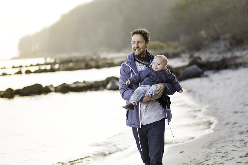 Father Holding Baby Walking Along Beach Shoreline