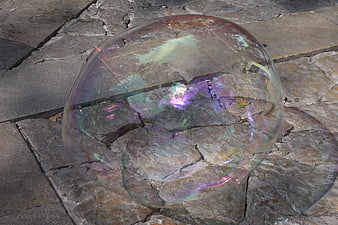 Large iridescent soap bubble resting on textured stone pavement