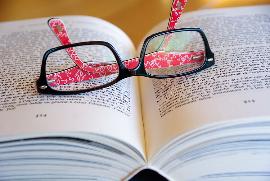 Black Eyeglasses with Red Straps on Open Book