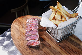 Sliced medium-rare steak and fries on wooden board