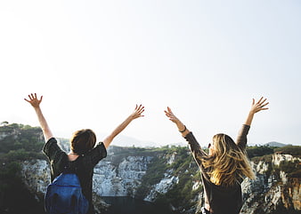 Two female friends raising arms in joy overlooking scenic canyon