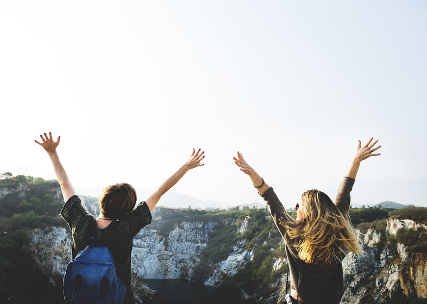 Two female friends raising arms in joy overlooking scenic canyon