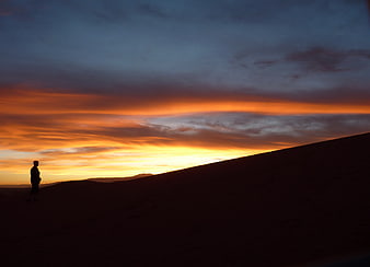 Silhouette of Person Standing on Sand Dune at Sunset