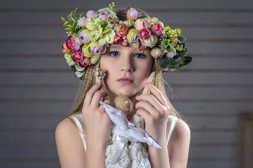 Portrait of young girl with floral wreath holding doll