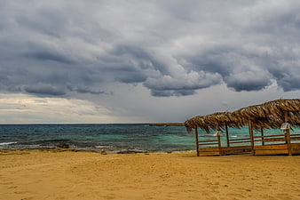 Empty Beach with Thatched Umbrellas Under Stormy Clouds