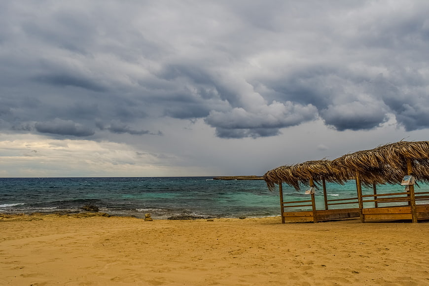 Empty Beach with Thatched Umbrellas Under Stormy Clouds