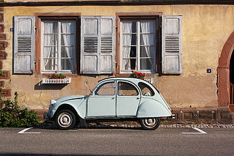 Vintage light blue car parked in front of rustic European building facade