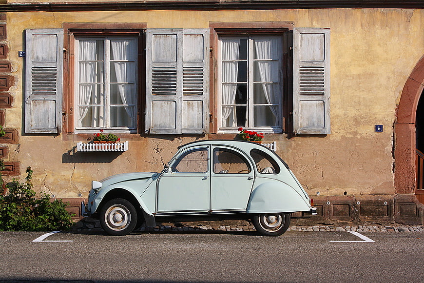 Vintage light blue car parked in front of rustic European building facade