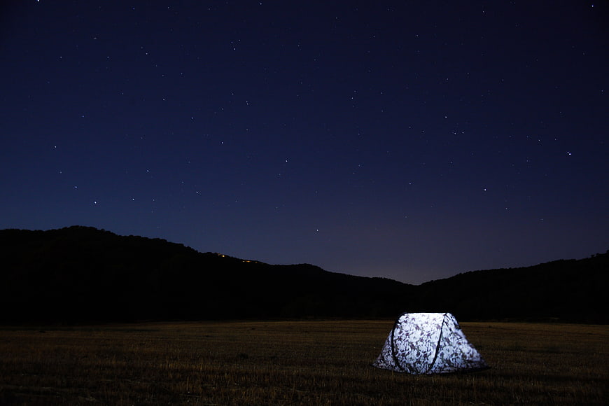 Illuminated Camping Tent Under Starry Night Sky in Field