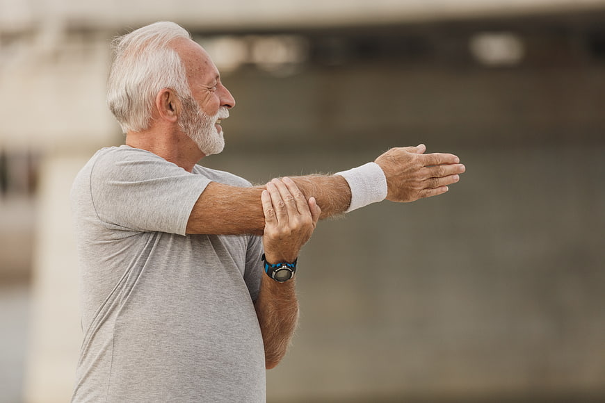 Senior man stretching arm outdoors for fitness