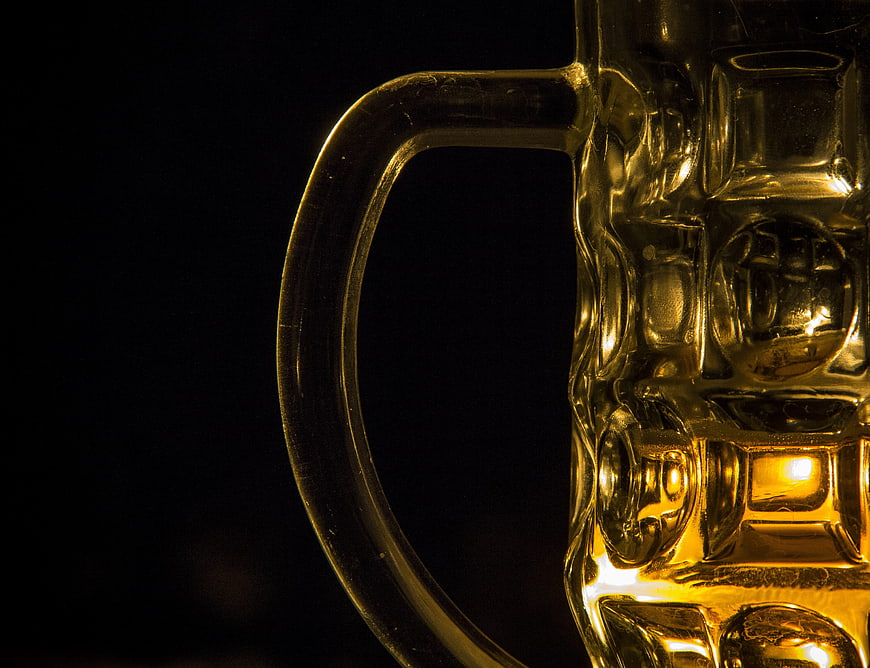 Close-up of golden beer in textured glass mug handle