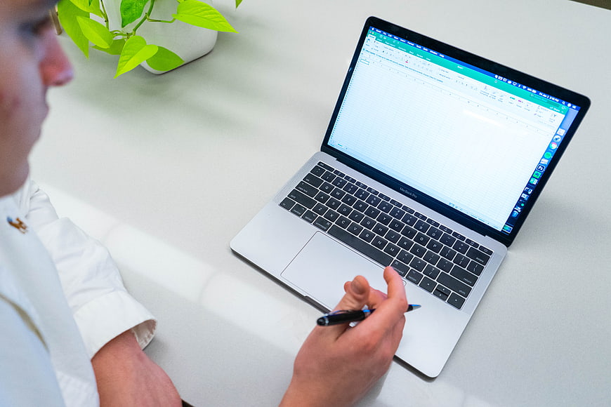 Man working on laptop with spreadsheet and pen