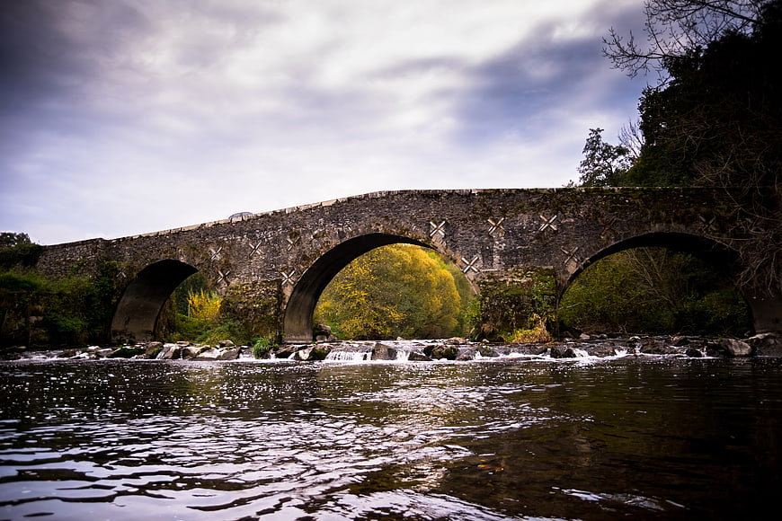 Historic stone arch bridge over flowing river with autumn foliage