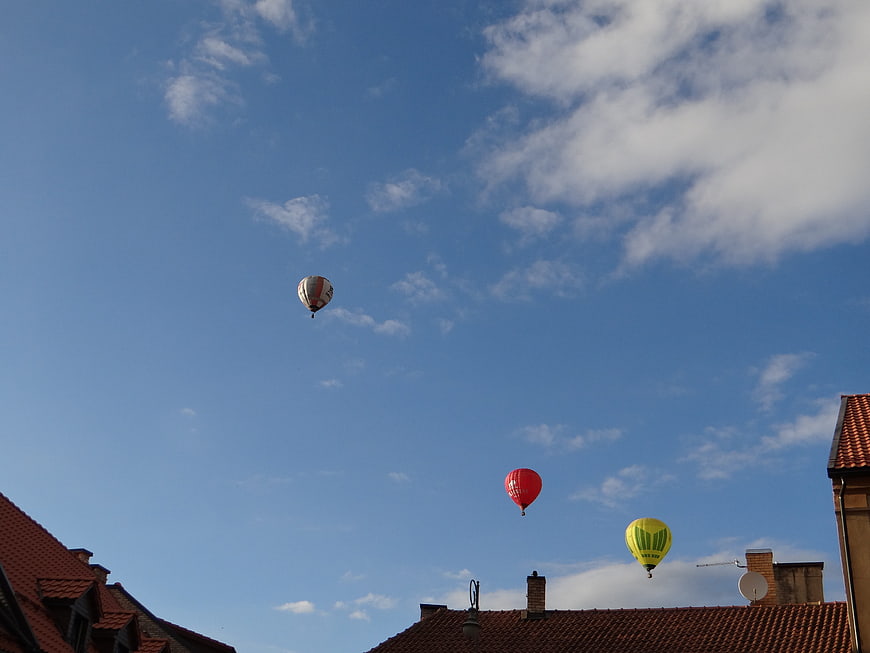 Hot air balloons floating over red tiled roofs under a blue sky