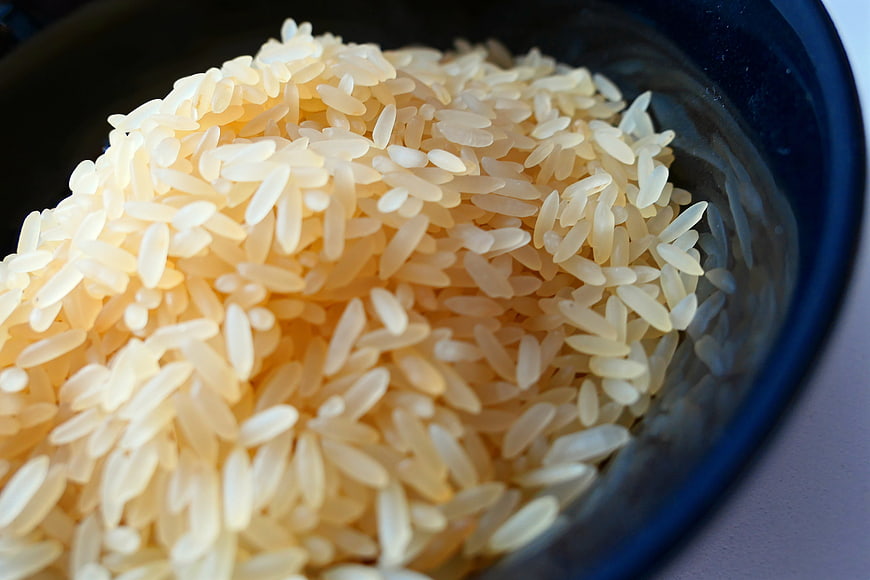 Close-up of uncooked white rice grains in a dark bowl
