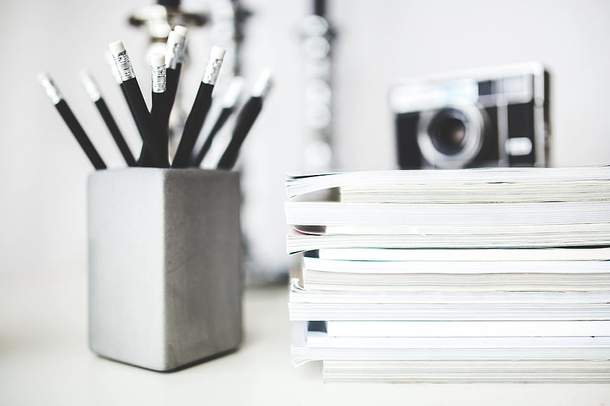 Stack of magazines and pencils in a gray cup on a desk